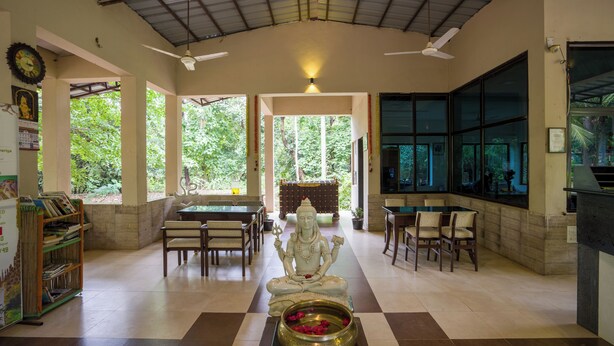 A spacious room with a large statue, a ceiling fan, and a dining area with chairs and tables.