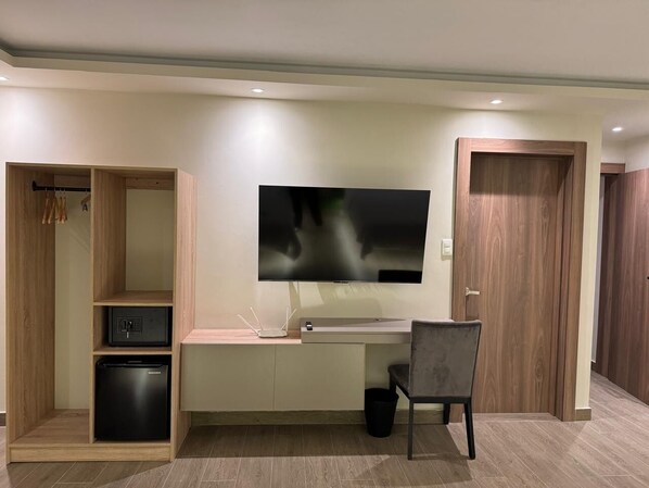 Habitación moderna con escritorio integrado, televisor de pantalla plana, armario, caja fuerte y cubo de basura.