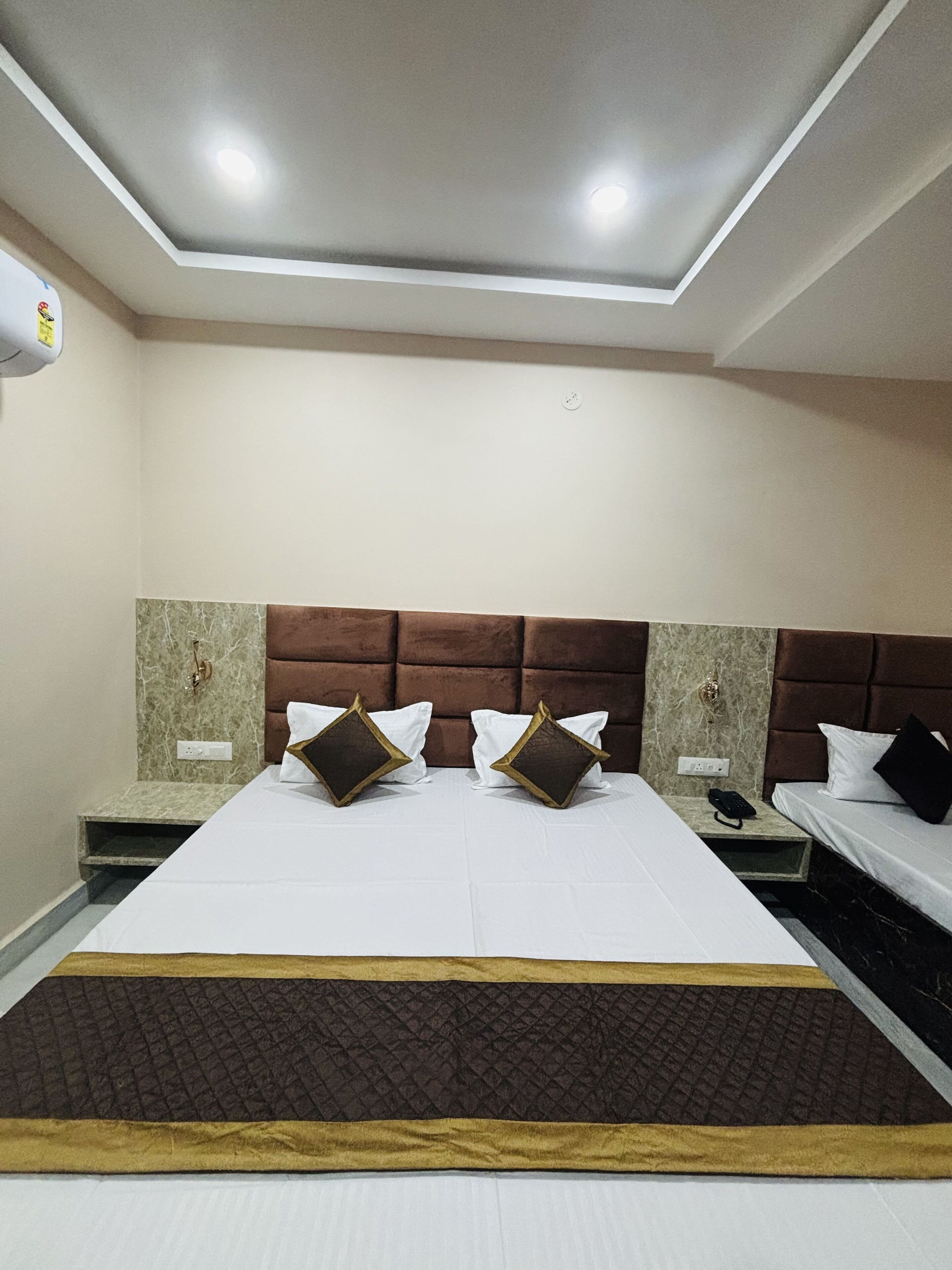 A hotel room with a large bed, two bedside tables, a headboard, and a ceiling light fixture.