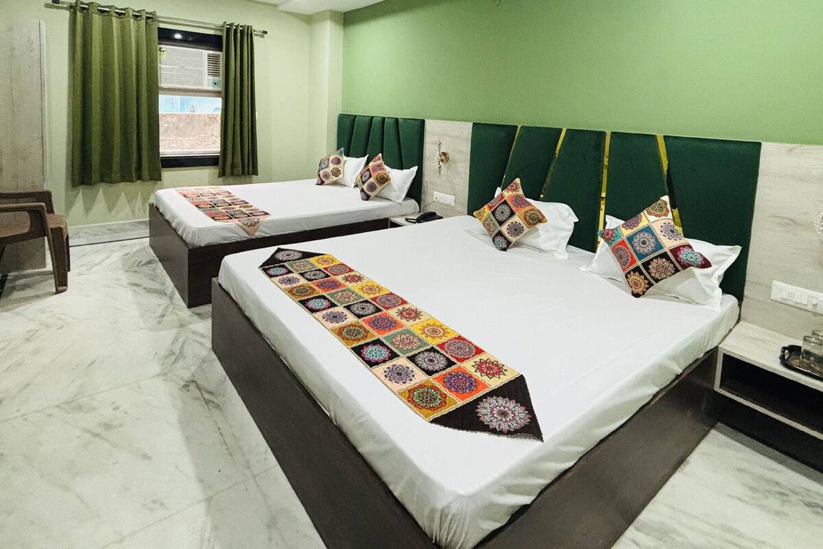 A hotel room with two beds, a wooden chair, a small table, and a window with curtains.