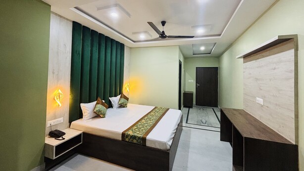 A bedroom with a bed, bedside tables, a desk, a ceiling fan, and a door. - Hotel Al Aziz (Ajmer)