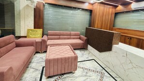 A modern interior with a sofa, ottoman, and a reception desk. - Hotel Al Aziz (Ajmer)