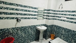 A bathroom with a white sink, a toilet, and a shower. There is a red bucket and a yellow cup on the floor. - Hotel Al Aziz (Ajmer)