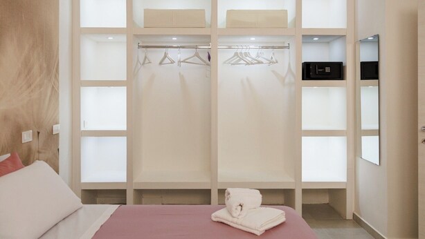 Een hotelkamer met een bed, een kledingkast met hangende kleding, een magnetron en een spiegel.