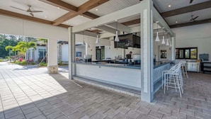 An outdoor bar area with a counter, bar stools, ceiling fans, and a view of a garden. - Stylish & Fun Retreat, Pool, Themed Rooms (Kissimmee)