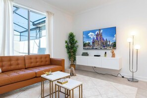 Uma sala de estar moderna com um sofá de couro, uma mesa de centro, uma TV fixada na parede, um abajur e uma janela grande.