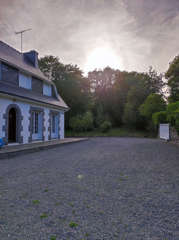 A two-story house with a gravel driveway and a stone wall.