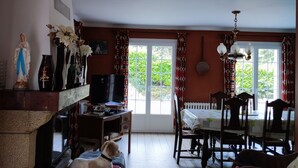 A living room with a fireplace, a television, a dining table with chairs, and a chandelier. - The little house in the forest (Clohars-Fouesnant)