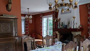 A dining room with a long table, chairs, a chandelier, and a fireplace. - The little house in the forest (Clohars-Fouesnant)