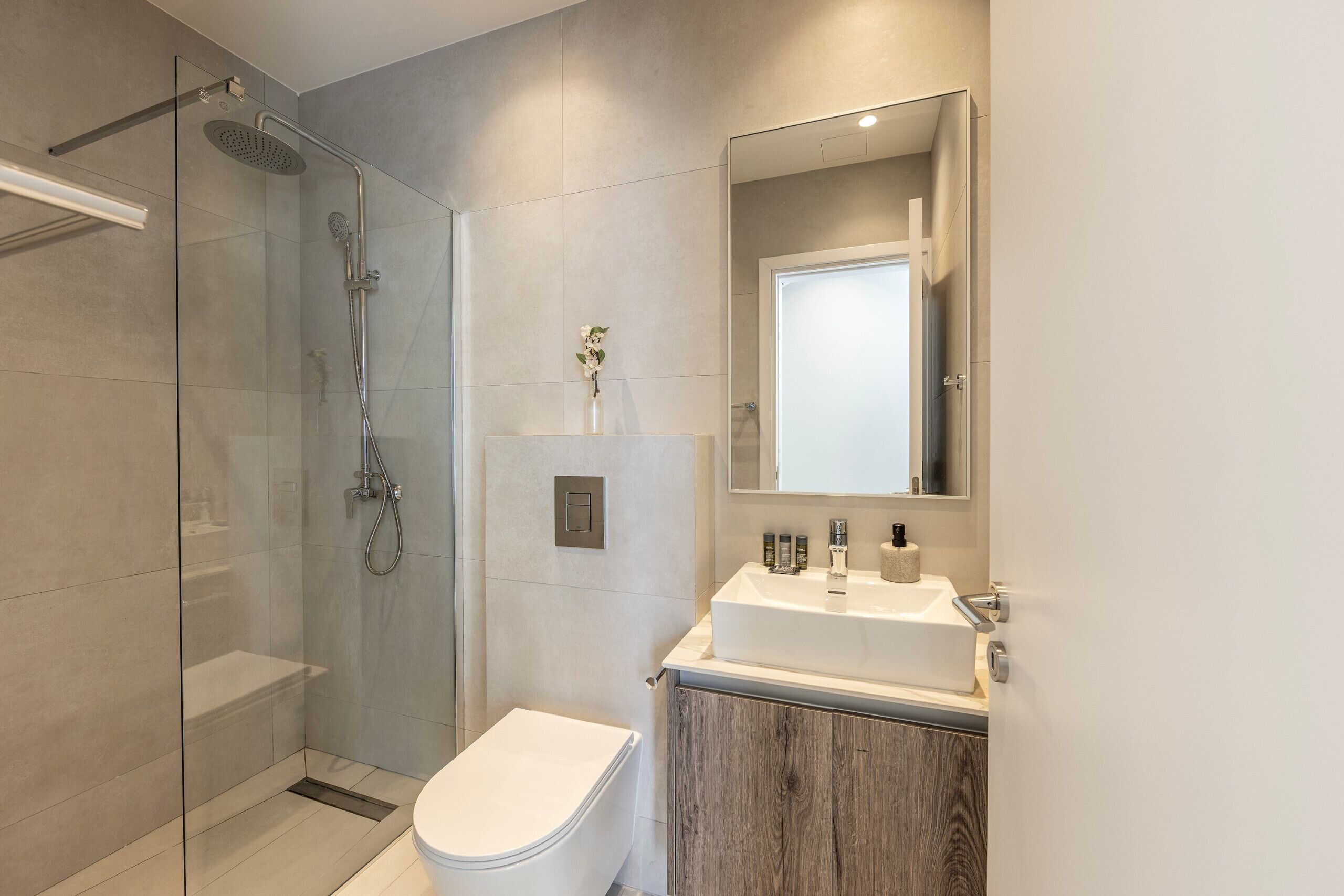 A modern bathroom with a glass-enclosed shower, a white toilet, and a wooden vanity with a mirror above the sink.