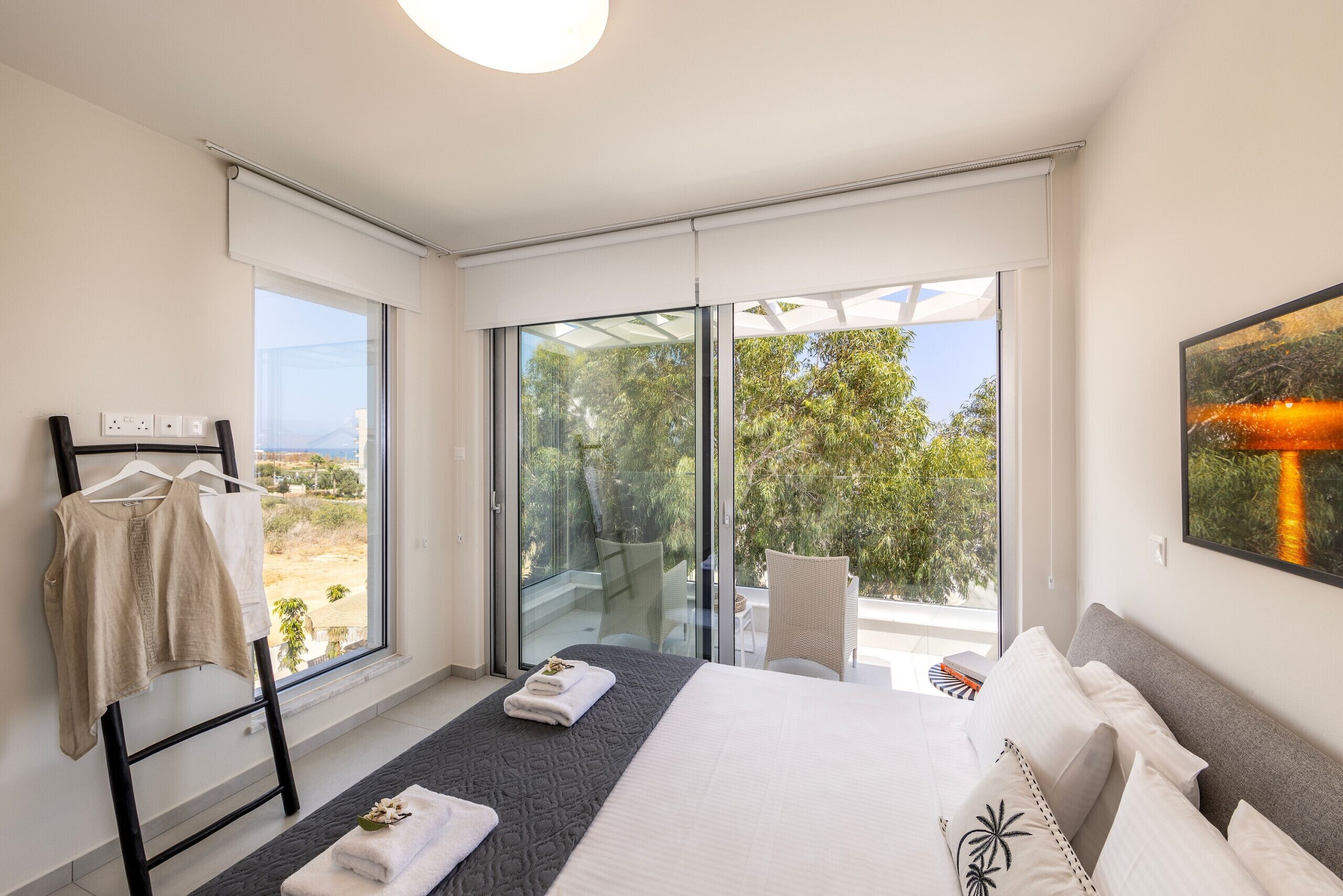 Une chambre moderne avec un grand lit, une porte vitrée donnant sur un balcon et une vue sur la verdure environnante.