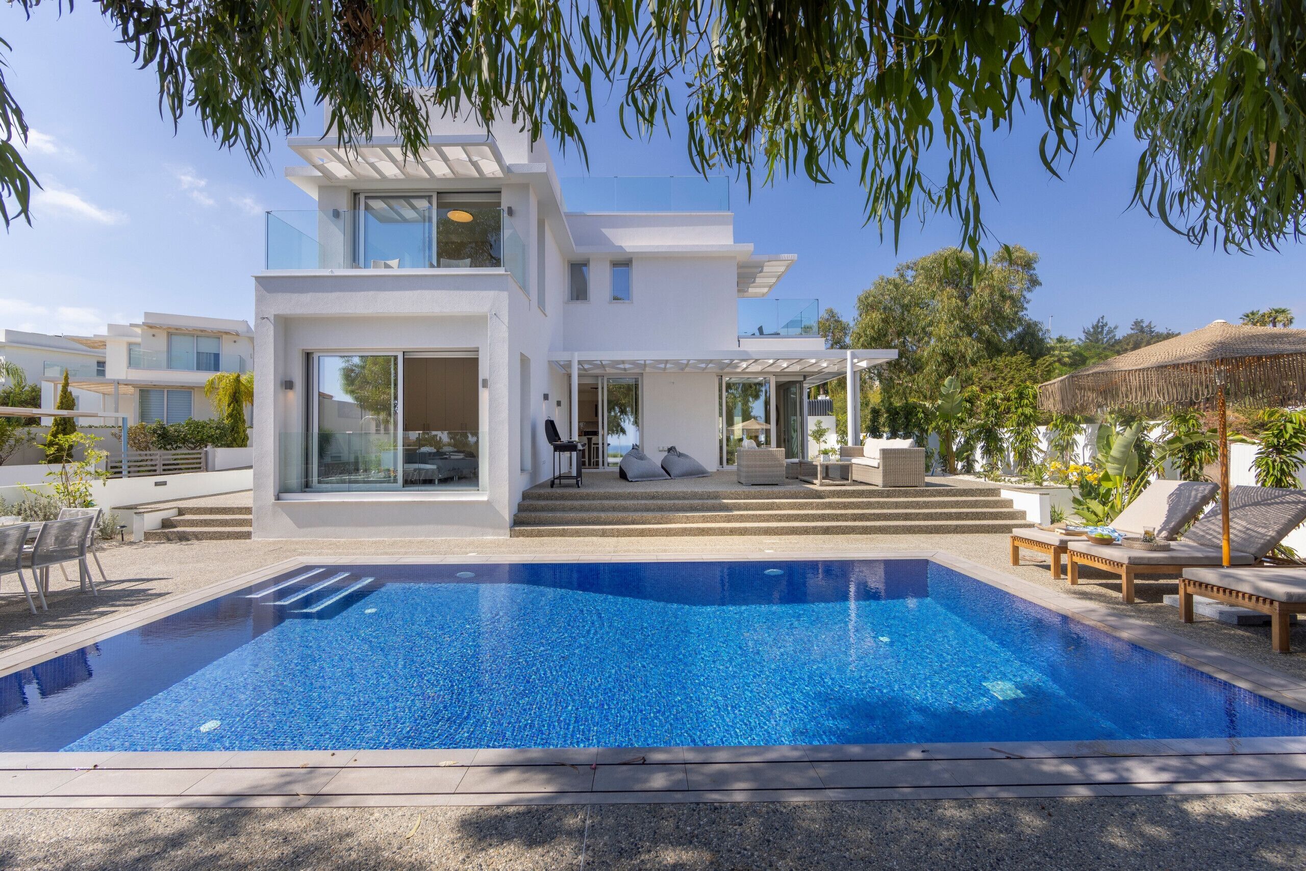 A modern two-story house with a swimming pool, outdoor seating, and a covered patio.
