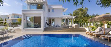 Una casa moderna de dos pisos con piscina, mobiliario exterior y un porche cubierto.