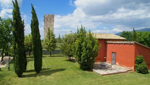 Un patio con un edificio rojo, una torre de piedra y altos cipreses.