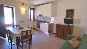 Cocina compacta con una mesa y sillas, un sofá verde y un televisor sobre un mueble de madera.