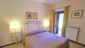 Un dormitorio con cama, dos mesitas de noche con lámparas, un radiador y una ventana con cortinas.