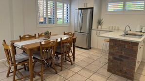Een moderne keuken met een centraal eiland, inbouwapparatuur en een eethoek met houten stoelen en een tafel.