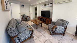 Een woonkamer met gestreepte banken, een houten salontafel, een televisie op een dressoir en een airconditioner aan de muur.