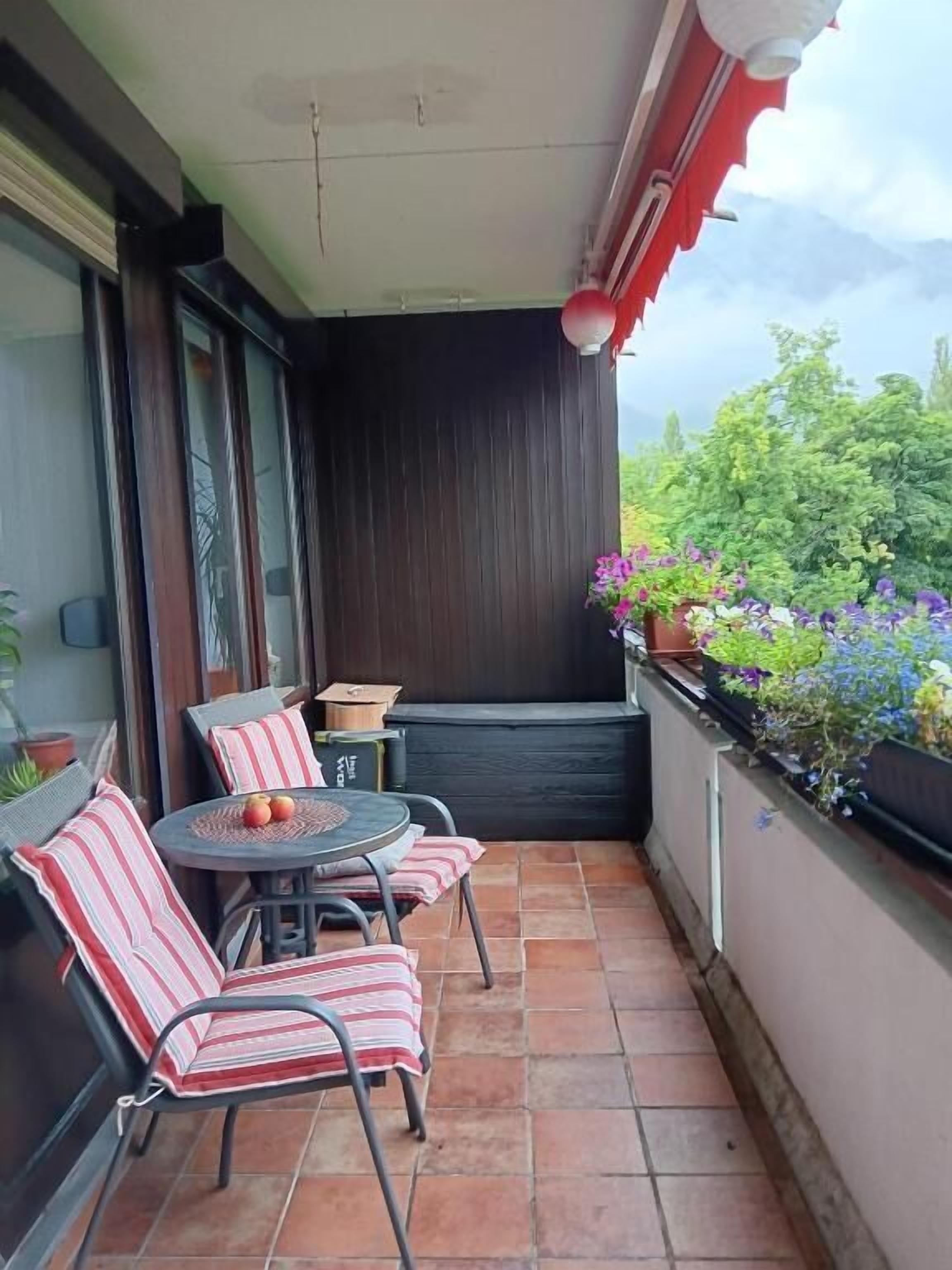Ein Balkon mit Tisch und Stühlen, einer Topfpflanze und Blick ins Grüne.