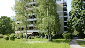 A multi-story residential building with balconies, surrounded by a well-maintained garden with various shrubs and a pathway. - Vacation apartment Lona, 1-3 pers., 45 sqm, living/bedroom (Bad Reichenhall)