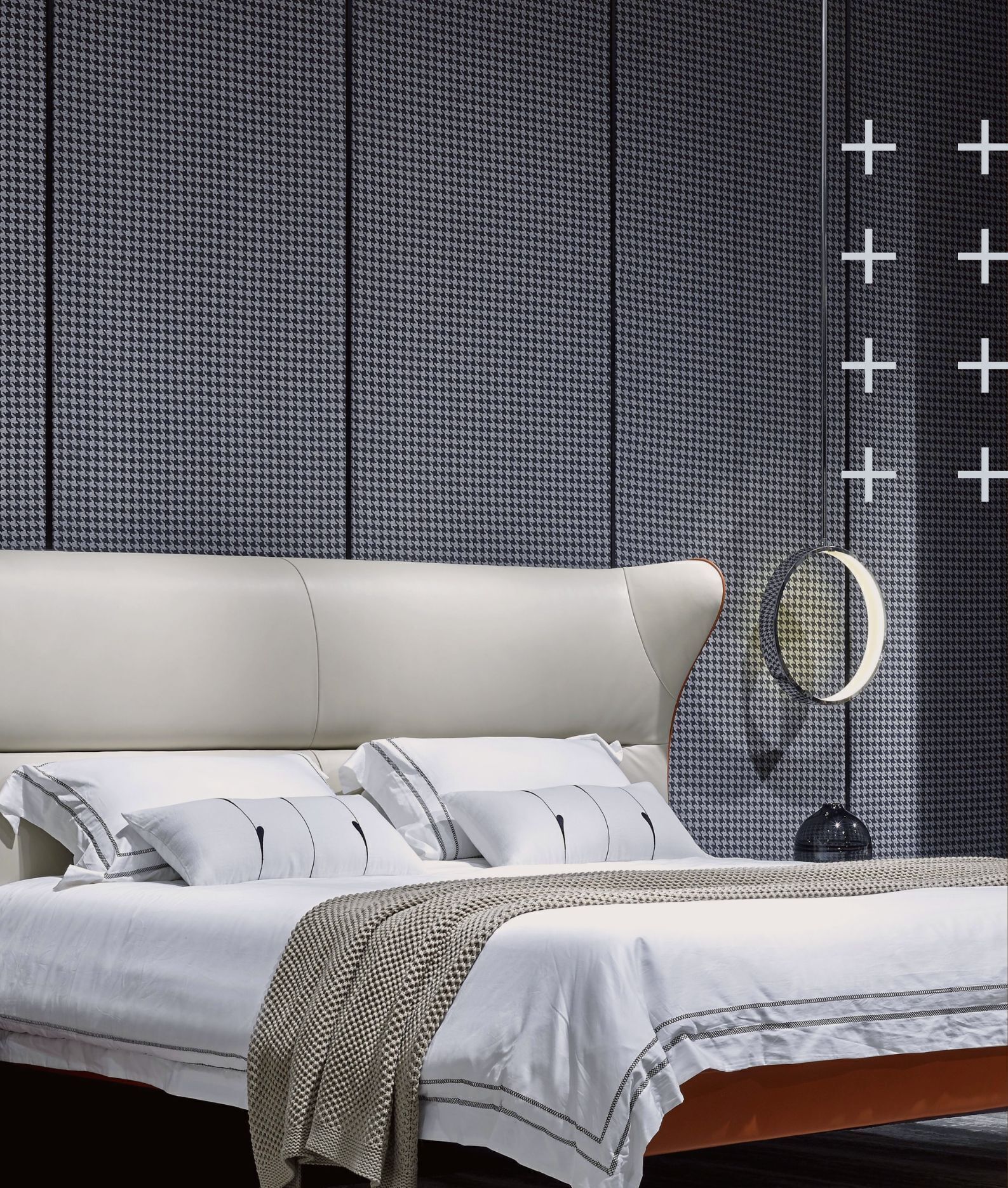 Ein modernes Schlafzimmer mit einem großen Bett, weißer Bettwäsche, einer Wand mit Hounds-Tooth-Muster und einem Spiegel mit rundem Rahmen.