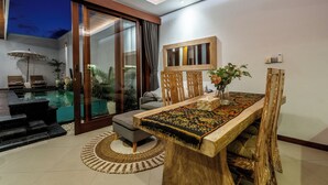 A modern dining area with a wooden table, cushioned chairs, and a glass partition. - Private Pool Villa Dacira by Orivista (Canggu)