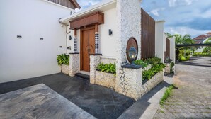A modern house with a stone facade, a wooden door, and a small garden area with plants. - Private Pool Villa Dacira by Orivista (Canggu)