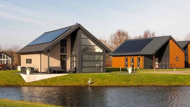 Un bâtiment moderne doté d’un toit en pente et de panneaux solaires, situé à proximité d’un plan d’eau où l’on peut apercevoir un cygne.