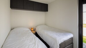 A bedroom with two single beds, a bedside table with a lamp, and a dark headboard. - Bungalow in Herkingen between nature reserve (Herkingen)