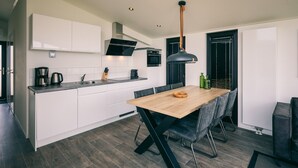 A modern kitchen with white cabinets, a wooden dining table, and black chairs. - Bungalow in Herkingen between nature reserve (Herkingen)