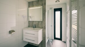 A modern bathroom with a white vanity, a large mirror, and a glass shower enclosure. - Bungalow in Herkingen between nature reserve (Herkingen)