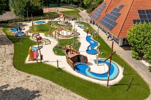 Ein Spielplatz mit verschiedenen Spielgeräten, darunter Rutschen und Kletterbereichen, umgeben von einem gepflegten Rasen.