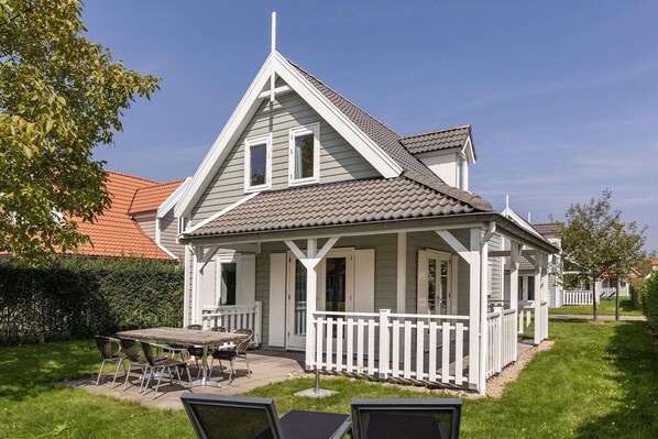 Ein zweistöckiges Haus mit Veranda, einem Essbereich mit Tisch und Stühlen sowie einem umzäunten Garten.