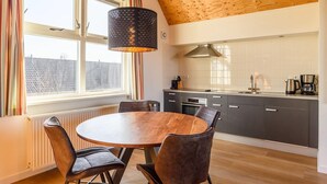 A modern kitchen with a round wooden table and chairs, a large window with curtains, and a wooden ceiling. - Waterfront escape with marina views (Terherne)