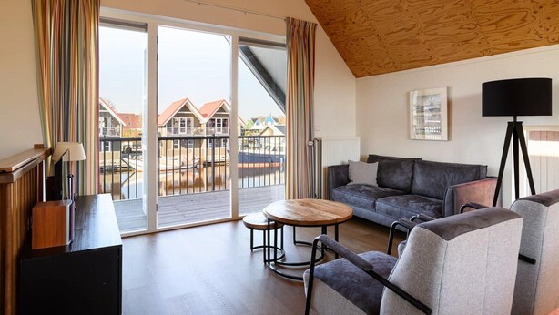 A modern living room with a wooden ceiling, a sofa, a coffee table, and a view of houses through large sliding doors. - Waterfront escape with marina views (Terherne)