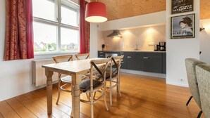 A modern kitchen with wooden cabinets, a dining table with chairs, and a red pendant light. - Waterfront escape with marina views (Terherne)