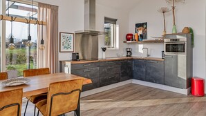 A modern kitchen with a dining area, large windows, and a view of the outdoors.