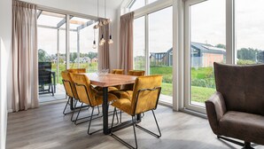 Un espace repas avec une table et des chaises en bois, de grandes fenêtres et une vue sur l’extérieur.