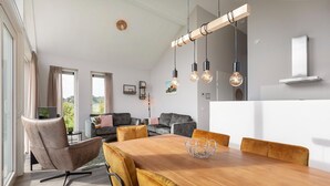 Un espace de salle à manger moderne avec une table en bois, des chaises rembourrées et des luminaires suspendus.