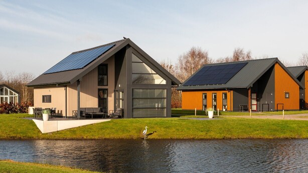 A modern building with a sloped roof and solar panels, adjacent to a body of water with a swan. - Tranquil villa for 6 guests with patio (Tynaarlo)