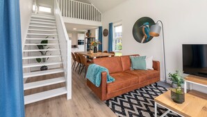 A modern living room with a staircase, a sofa, a coffee table, and a TV. - Tranquil villa for 6 guests with patio (Tynaarlo)