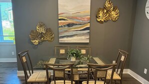 A dining area with a glass-top table surrounded by six wooden chairs with cushioned seats.