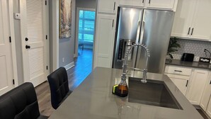 A modern kitchen with a large island, stainless steel appliances, and a seating area with black chairs.