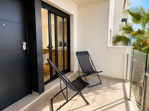 Ein Balkon mit zwei schwarzen Stühlen, einer Schiebetür und Blick auf eine Palme.