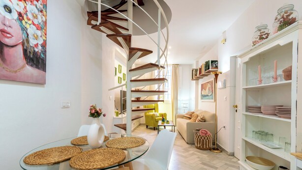 A modern interior with a spiral staircase, a dining area with glass table and woven placemats, and a white cabinet with glassware. - Virgen de la Luz. 2-bedrooms, 2-bathrooms (Sevilla)