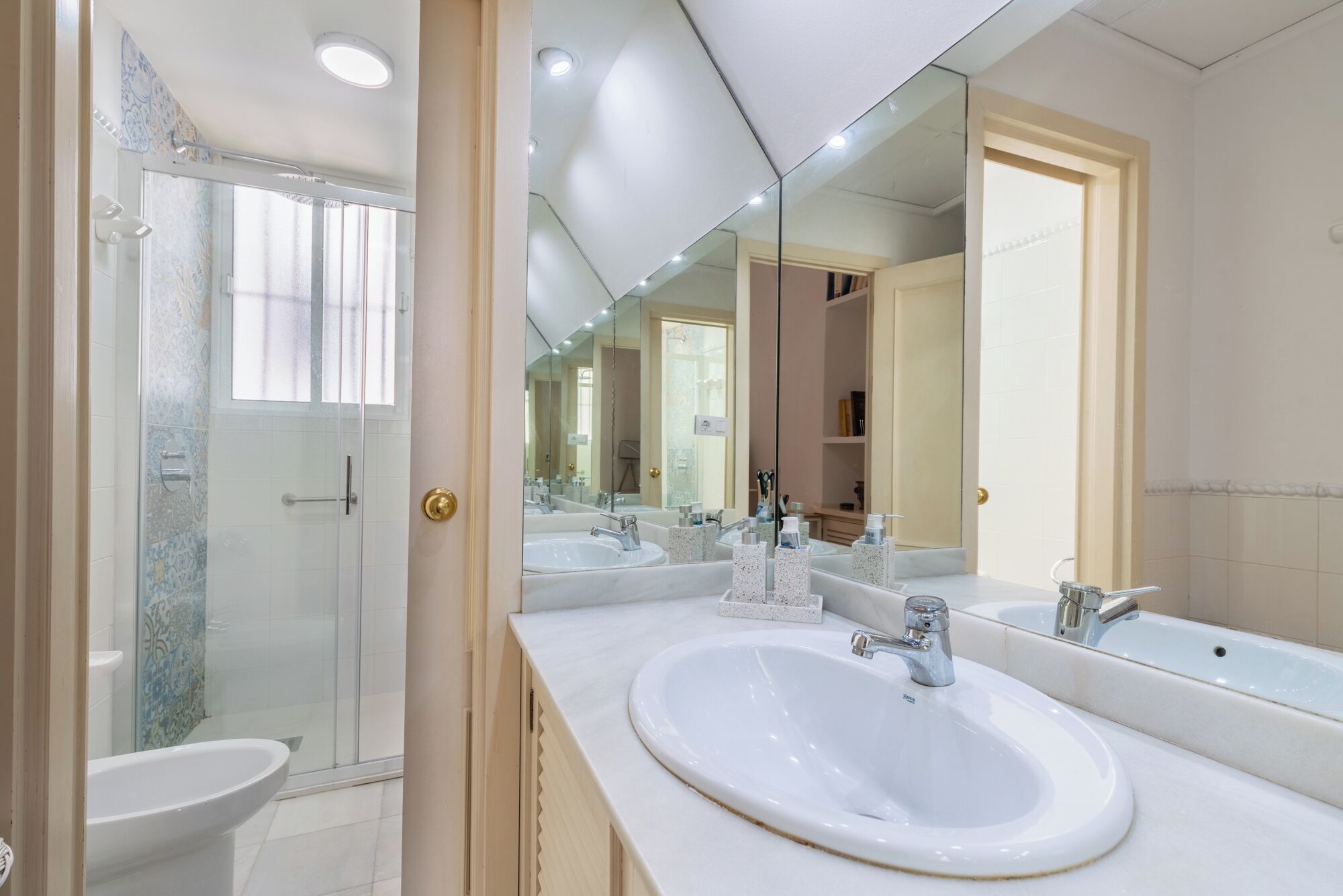 A modern bathroom with a large mirror, two sinks, and a shower area.