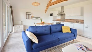 A modern living room with a blue sofa, a round table with a fruit centerpiece, and a kitchen in the background. - Stylish Comfort by the Opal Coast (Berck-Sur-Mer)