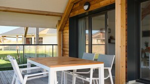 An outdoor wooden deck with a table and chairs, a glass door leading to a room, and a view of neighboring houses. - Stylish Comfort by the Opal Coast (Berck-Sur-Mer)