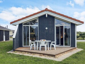 A modern house with a deck, large windows, and a dining area with chairs. - 4 Star Holiday Home in Friedrichkoog (Friedrichskoog)