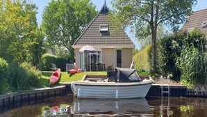 A canal with a house and a boat docked nearby. - Water villa with outdoor spa, jetty (Eernewoud)